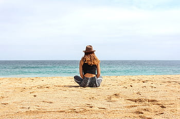 A woman seated on a sunny beach, gazing at the calm ocean horizon, embodying serenity and escape. HD wallpaper