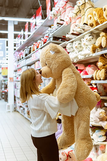 A woman chooses a large teddy bear in a retail toy section, surrounded by stuffed animals. HD phone wallpaper