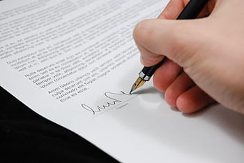 Close-up of a hand signing a legal document with a fountain pen, symbolizing signature and agreement. HD wallpaper