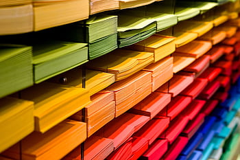 Vibrant multicolored paper stacks arranged on shelves in a stationery store. HD wallpaper