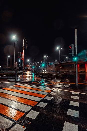 A city street at night with wet pavement reflecting streetlights and traffic signals. HD phone wallpaper