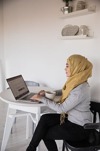 Middle Eastern woman in hijab using a laptop at home. Comfortably seated with coffee. HD phone wallpaper