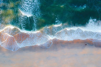 Stunning aerial shot capturing waves crashing onto a serene sandy beach. HD wallpaper