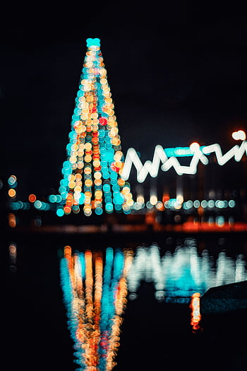 Blurred Christmas tree lights reflect in water at night, creating a festive ambiance. HD phone wallpaper