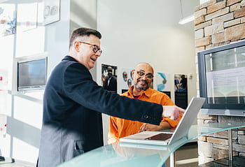 Two businessmen having a lively discussion in a modern office setting, pointing at a laptop screen. HD wallpaper