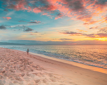 Tranquil sunset view on a Hawaiian beach with a lone person walking along the shoreline. HD wallpaper