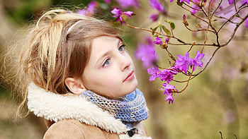 Pretty Cute Little Girl Is Standing Near Purple Flowers Tree Branches In Blur Background Wearing Brown Overcoat Woolen Knitted Scarf Cute HD wallpaper