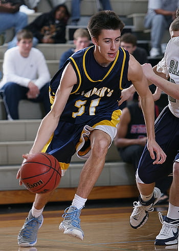 Teen basketball player dribbling during an intense game in a school gym. HD phone wallpaper