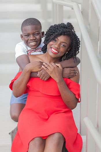 A cheerful African American mother and son share a loving hug on a staircase, both smiling brightly. HD phone wallpaper