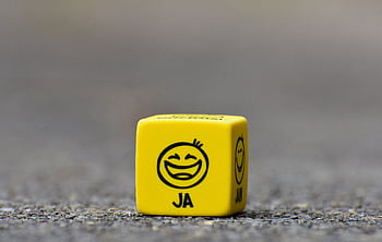 Close-up of a yellow dice featuring a smiley face emoticon symbolizing happiness and fun. HD wallpaper