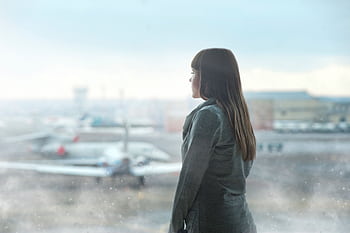 A woman gazing at airplanes through a window at Kyiv's airport terminal, capturing a moment of reflection. HD wallpaper