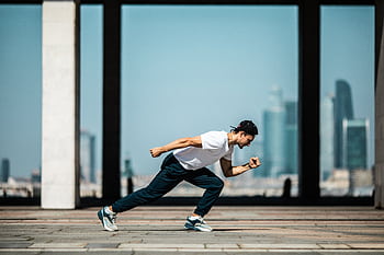 Dynamic shot of a young man sprinting outdoors in an urban setting with skyscrapers in the background. HD wallpaper