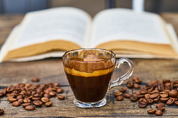 A rich espresso cup surrounded by beans and an open book, perfect for a relaxing break. HD wallpaper