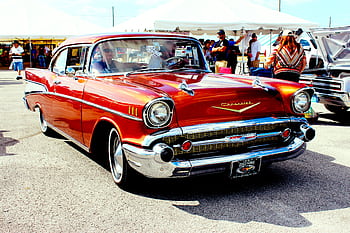 A vintage red 1957 Chevrolet showcased at an outdoor car exhibition with attendees. HD wallpaper