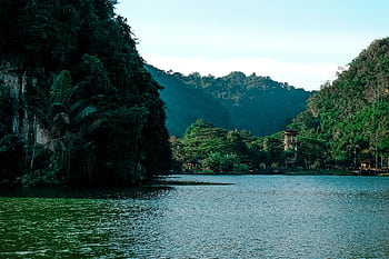 A tranquil lakeside view surrounded by lush forests and towering mountains under a clear sky. HD wallpaper