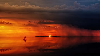 A tranquil seascape with a sailing boat at sunset, reflecting on calm waters. HD wallpaper