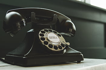Classic black rotary on hotel reception desk, evoking nostalgia and vintage charm. HD wallpaper