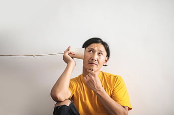 A thoughtful man in a yellow shirt uses a paper cup . White background, concept of communication and contemplation. HD wallpaper