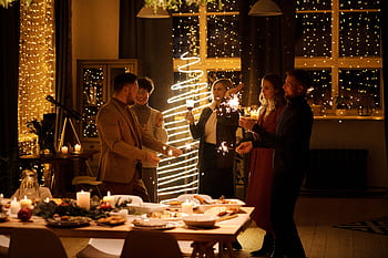 Group of adults celebrating Christmas indoors with sparklers and festive decor. HD wallpaper