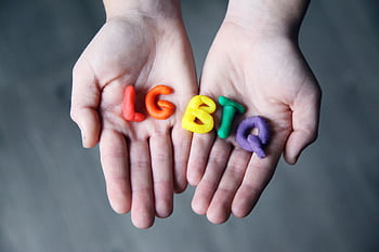 Close-up of hands holding colorful letters representing LGBTQ pride. HD wallpaper