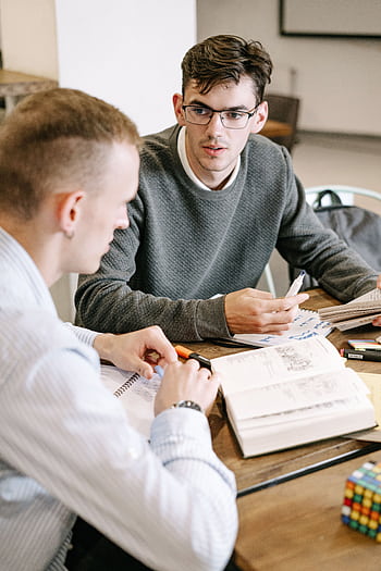 Two young men studying together at a table with books and notes. HD phone wallpaper