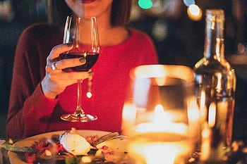 A woman enjoying red wine at a romantic candlelit dinner, perfect for celebrations. HD wallpaper
