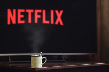 A steaming mug on a table in front of a TV displaying Netflix, creating a cozy indoor atmosphere. HD wallpaper