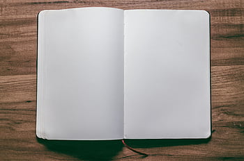 A top-down view of an open blank notebook on a wooden desk, perfect for design or writing projects. HD wallpaper