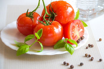 A fresh and vibrant display of tomatoes, basil, and peppercorns on a white plate, perfect for healthy cooking. HD wallpaper