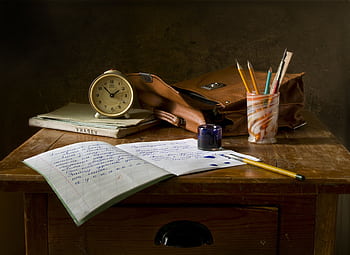Classic wooden desk with writing materials, vintage clock, and a leather bag. HD wallpaper