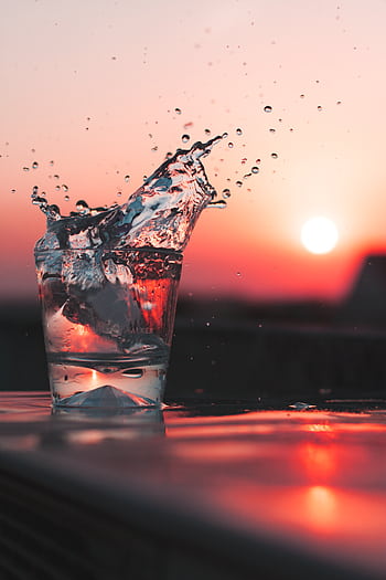 Dramatic splash of water in a glass against a vibrant sunset backdrop. Perfect for refreshment themes. HD phone wallpaper