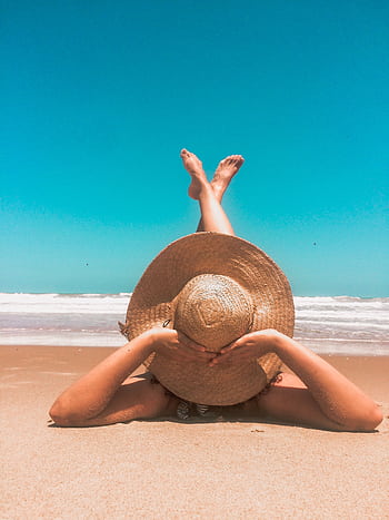 A woman in a straw hat relaxes on a sunny beach, enjoying the clear blue sky and ocean waves. HD phone wallpaper