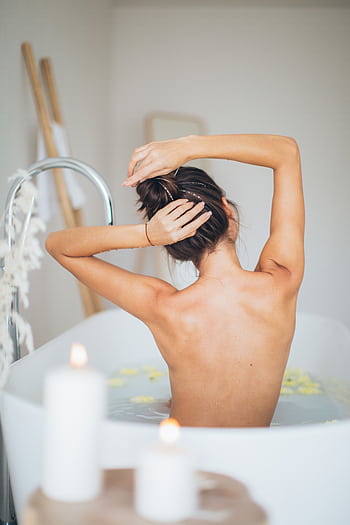 A woman enjoying a relaxing bath surrounded by candles and petals for a soothing spa experience. HD phone wallpaper