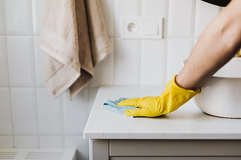 Close-up of a person wearing yellow gloves wiping a bathroom counter with a cloth. HD wallpaper