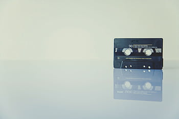 Retro cassette tape on a reflective surface, evoking nostalgia and vintage music vibes. HD wallpaper