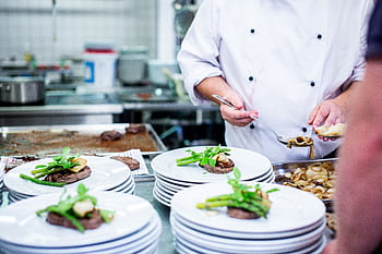 A chef prepares gourmet dishes in a professional kitchen setting, showcasing fine dining elegance. HD wallpaper