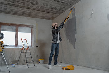 A man painting an interior wall with a roller during a home renovation project. HD wallpaper