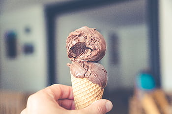 Close-up of a hand holding a chocolate ice cream cone indoors. HD wallpaper