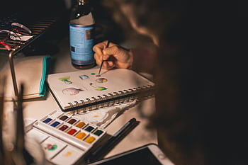 Artist painting with watercolors in a notepad at a desk. Creative process indoors. HD wallpaper