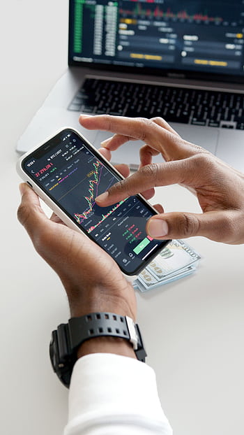Hands using smart trading app with charts, dollar bills in background. HD phone wallpaper