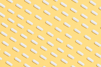 Pattern of white capsules on a bright yellow surface, symbolizing healthcare and medicine. HD wallpaper