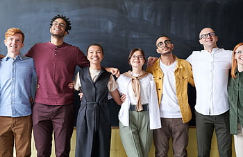 A diverse group of colleagues joyfully embracing in an office setting, showcasing team spirit. HD wallpaper