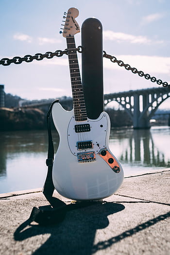 Electric guitar resting by the riverside with a bridge in the background, under daylight. HD phone wallpaper