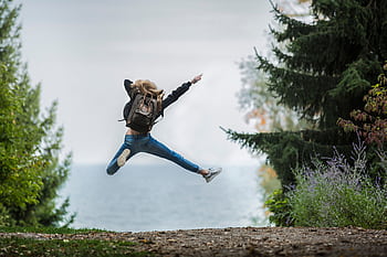 Energetic woman leaping in outdoor forest setting with lake view, showcasing dom and joy. HD wallpaper