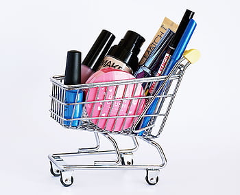 Miniature shopping cart filled with a variety of cosmetics on a white background. HD wallpaper