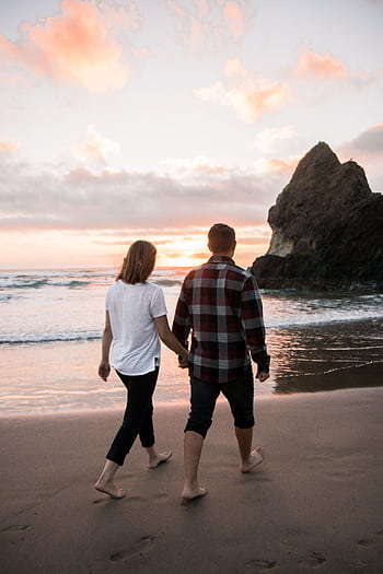 A couple holding hands while walking on a scenic beach at sunset, creating a romantic atmosphere. HD phone wallpaper