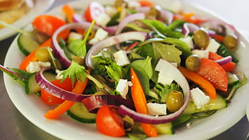 A vibrant Mediterranean salad featuring fresh vegetables, olives, and feta cheese for a healthy meal. HD wallpaper