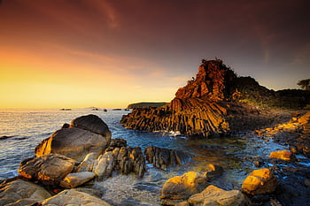 A serene rocky seascape at sunset with golden hues reflecting on the water and rocks, creating a tranquil atmosphere. HD wallpaper