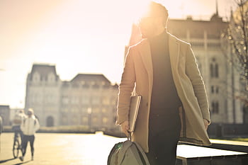 A businessman walks in front of a historic building in Budapest with sun glare illuminating the scene. HD wallpaper