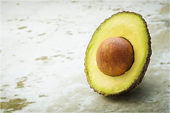 Close-up of a ripe avocado half with seed, showcasing its vibrant green flesh on a soft textured background. HD wallpaper